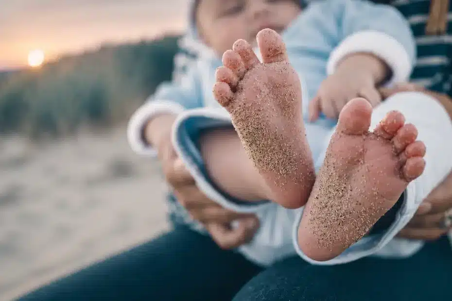 Babyfüße im Sand auf dem Schoß der Eltern – Symbol für Geburtstrauma, frühe Bindungserfahrungen, vorgeburtliche Prägungen und die Auswirkungen von Trauma auf Körper und Nervensystem.