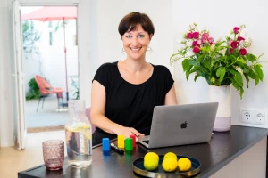 Psychotherapeutin Julia Belke arbeitet am Laptop in heller Praxis mit Blumen und bunten Klötzen